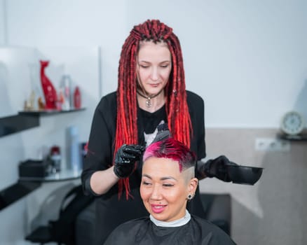 The hairdresser dyes the hair of an Asian woman in pink. Short extreme haircut