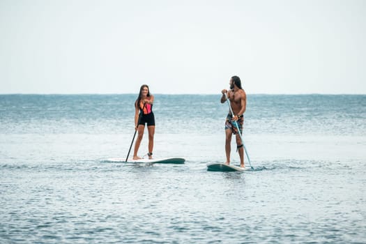 Sea woman and man on sup. Silhouette of happy young woman and man, surfing on SUP board, confident paddling through water surface. Idyllic sunset. Active lifestyle at sea or river