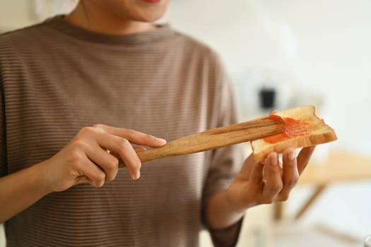 Woman spreading raspberry jam on toasted bread. People, food and domestic life concept.