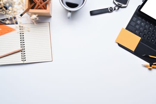 White office desk with laptop, cup of coffee, notepad and stationery. Top view with space for text.