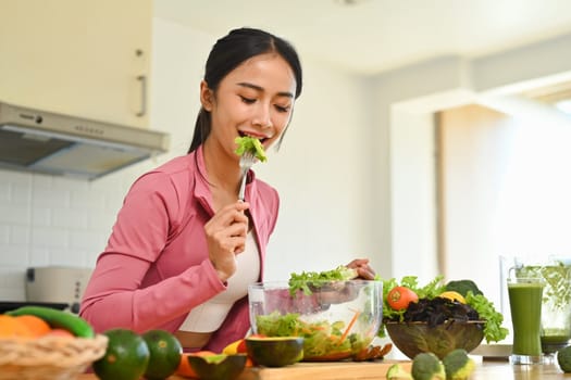 Attractive young woman eating healthy vegetable salad in kitchen. Healthy lifestyle concept.
