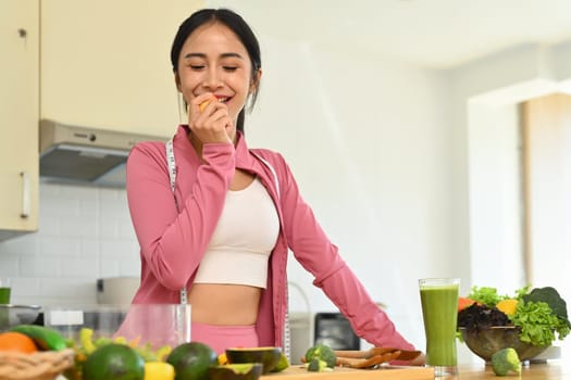 Beautiful young woman eating apple in the kitchen. Health lifestyle and nutrition concept.