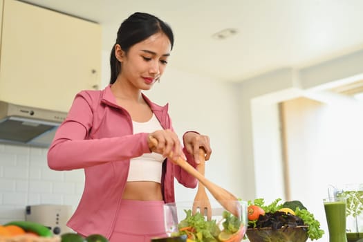 Young sporty woman making vegetable salad in kitchen. Dieting, health lifestyle and nutrition concept.
