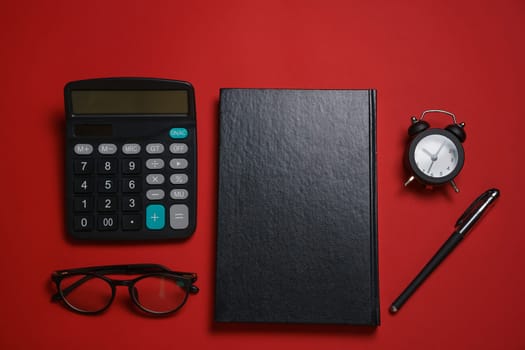 Male black notepad ballpoint pen and calculator, small alarm clock and glasses on dark red background, business concept