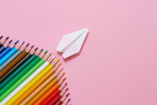 Paper plane, wood colored pencils, flat dip on pink background, top view. A true school concept, in the form of a corner. Pastel color