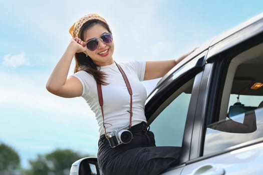 Happy young woman on summer road trip, leaning out car window. Travel, journey, nature and lifestyle concept.