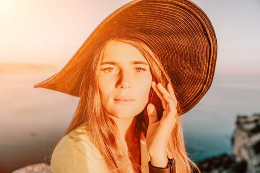 Portrait of happy young woman wearing summer black hat with large brim at beach on sunset. Closeup face of attractive girl with black straw hat. Happy young woman smiling and looking at camera at sea