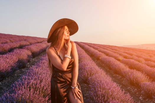 Close up portrait of young beautiful woman in a white dress and a hat is walking in the lavender field and smelling lavender bouquet.