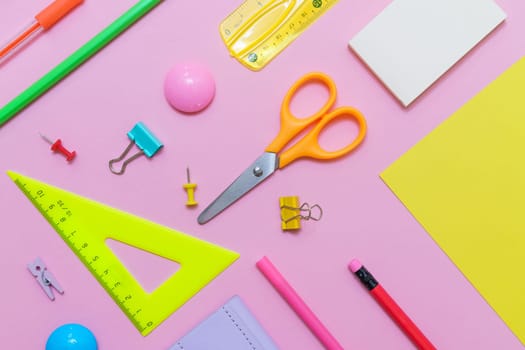 White notepad on spring and stationery school supplies on a pink background, heaps of colored pencils, paper clips, multi-colored objects for work and creativity, back to school