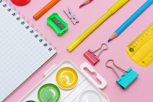 White notepad on spring and stationery school supplies on a pink background, heaps of colored pencils, paper clips, multi-colored objects for work and creativity, back to school