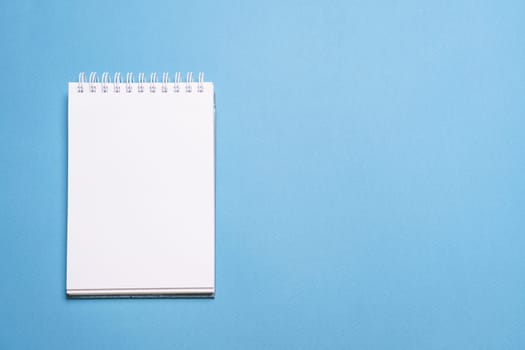 School notebook on blue background, spiral notepad on table, education and business concept