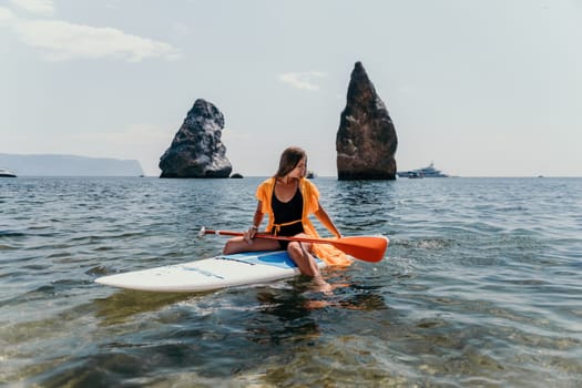 Close up shot of beautiful young caucasian woman with black hair and freckles looking at camera and smiling. Cute woman portrait in a pink bikini posing on a volcanic rock high above the sea