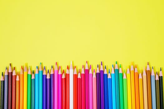 Assortment of colored pencils in various iridescent colors on a yellow background