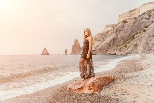 Side view a Young beautiful sensual woman in a mint long dress posing on a volcanic rock high above the sea during sunset. Girl on the nature on overcast sky background. Fashion photo