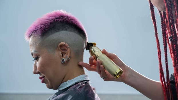 The hairdresser shaves the back of the head of a female client. Rear view of a woman with short pink hair in a barbershop