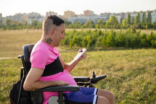 Disabled gay man sits in a wheelchair and uses a mobile phone working online.