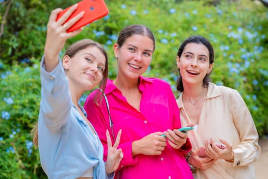 Three smiling women posing for a selfie in a lush green park. They embrace each other, expressing happiness and friendship. The vibrant colors and natural background create a joyful atmosphere.