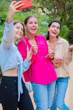 Three smiling women posing for a selfie in a lush green park. They embrace each other, expressing happiness and friendship. The vibrant colors and natural background create a joyful atmosphere.