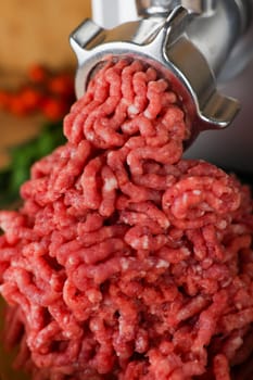 The concept of healthy and proper nutrition, cooking. Close-up view from above of red ground beef with streaks of fat coming out of a metal meat grinder. High quality photo