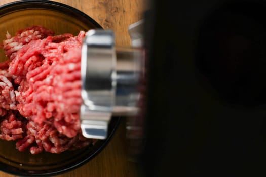The concept of healthy and proper nutrition, cooking. Top and left view of red ground beef with streaks of fat coming out of a metal grinder with space for text on the right on a black background. High quality photo