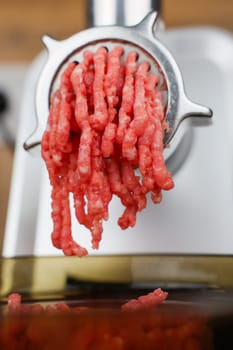 The concept of healthy and proper nutrition, cooking. Close-up side view of red ground beef with streaks of fat coming out of a metal grinder and falling into a transparent black plate below. High quality photo