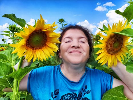 A woman smiles happily while holding sunflowers in a blooming field. The bright yellow petals contrast beautifully against the clear blue sky.