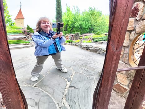 Blonde woman has fun taking a silly selfie in a distorted mirror while exploring a park filled with lush greenery.