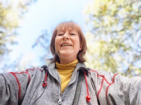 Blonde woman in a gray sweater smiles widely as she takes a selfie during her autumn adventure in nature.