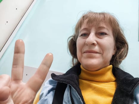 Middle-aged woman smiles and poses for a selfie, capturing a moment of joy and relaxation at home in a colorful outfit