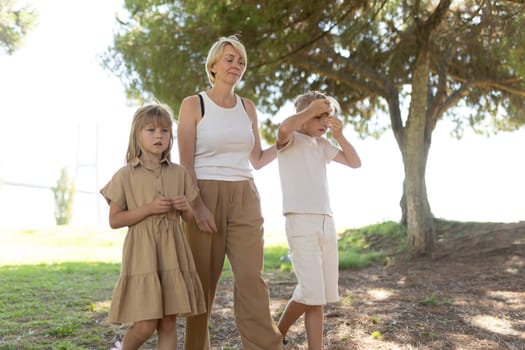 Mother and her two children walking in a park under a tree during a summer day