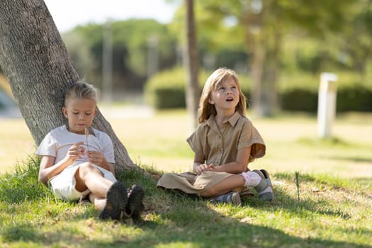 Two kids relaxing and playing under a tree on a sunny day