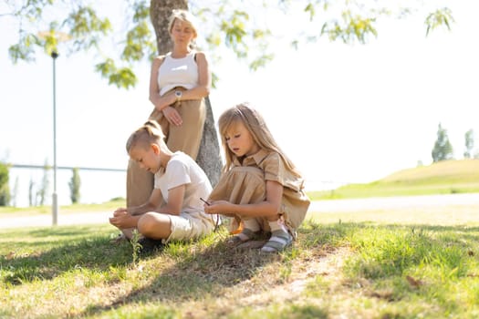 Two children and an adult enjoying a sunny day under a tree