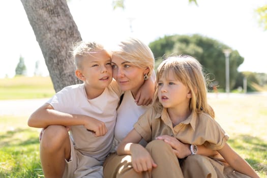 Mother and her two children relaxing under a tree in a sunny park