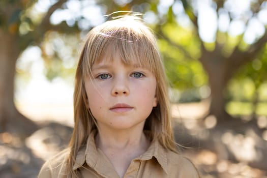 Child standing outdoors under large trees on a sunny day