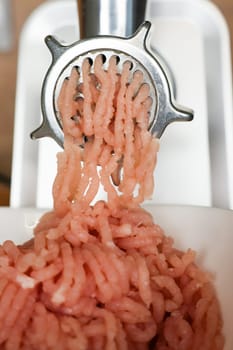 Close-up of pink minced turkey coming out of a metal meat grinder into a white plate. The concept of dietary recipes, proper and healthy nutrition, the cooking process. High quality photo
