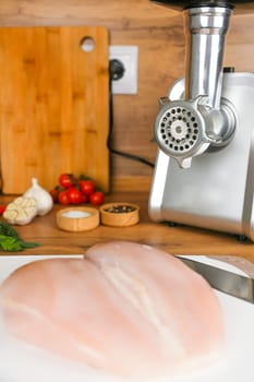 Chicken fillet lies on a white cutting board against the background of a meat grinder, vegetables and spices. The concept of dietary recipes, proper and healthy nutrition, the cooking process. High quality photo