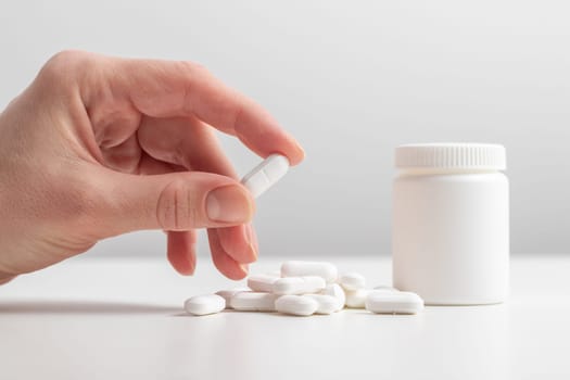 Female taking medicine, holding white pill and a glass of water on white background. Concept of health care, dietary supplements, treatment of depression and diseases. High-quality photo
