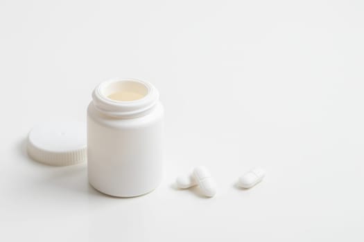 White pills and plastic medicine bottle on a white background with copy space. Medicine and health concepts include a jar with pills or vitamins. High-quality photo mock-up banner