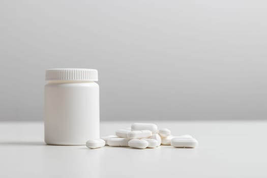 White pills and plastic medicine bottle on a white background with copy space. Medicine and health concepts include a jar with pills or vitamins. High-quality photo mock-up banner