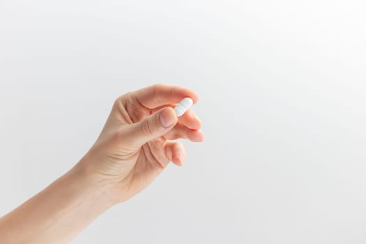 Female taking medicine, holding white pill and a glass of water on white background. Concept of health care, dietary supplements, treatment of depression and diseases. High-quality photo