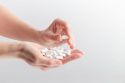 Female taking medicine, holding white pill and a glass of water on white background. Concept of health care, dietary supplements, treatment of depression and diseases. High-quality photo
