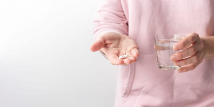 Female taking medicine, holding white pill and a glass of water on white background. Concept of health care, dietary supplements, treatment of depression and diseases. High-quality photo