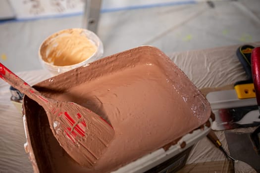This is a closeup view of a paint tray filled with rich brown paint and a wooden spatula, ideal for all DIY projects