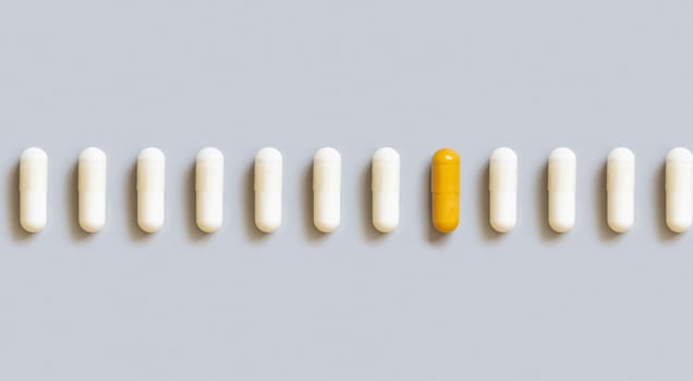 Beige medical capsules in a line with yellow one in the middle on grey top view. Preventive medicine and healthcare, dietary supplements and vitamins. Assorted alternative medicine capsules