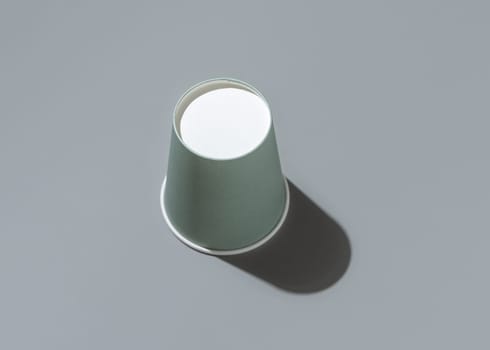 Disposable light green paper cups on a grey n background with hard shadow top view, mockup with advertising copy space. Empty cardboard coffee cup. No plastic and sustainable lifestyle concept