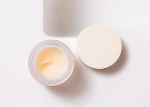 Opened lip balm jar with blank lid on white washbasin top view, cosmetic packaging mockup, copy space. Lipcare beauty product for everyday personal care or spa procedures