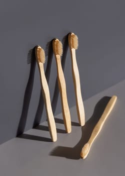 Biodegradable bamboo toothbrushes on a grey two tones background with hard shadow closeup, mockup, negative space. Natural personal accessories for dental care, minimal style aesthetic