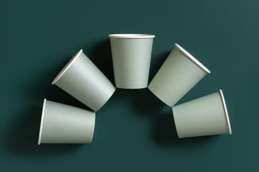Disposable light green paper cups on a dark green background top view, mockup with advertising copy space. Empty cardboard coffee cups flat lay. No plastic and sustainable lifestyle concept