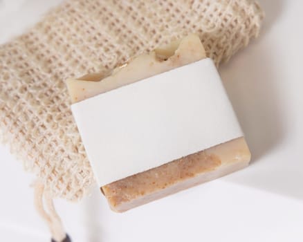 Beige handmade soap bar with blank label on sisal soap saver bag on washbasin close up, packaging mockup, copy space. Natural herbal unbranded product for daily hygiene