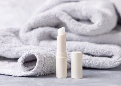 Opened white blank lip balm stick with a lid near light gray bath towel closeup, cosmetic mockup. Lifestile scene with Lipcare beauty product for daily personal care